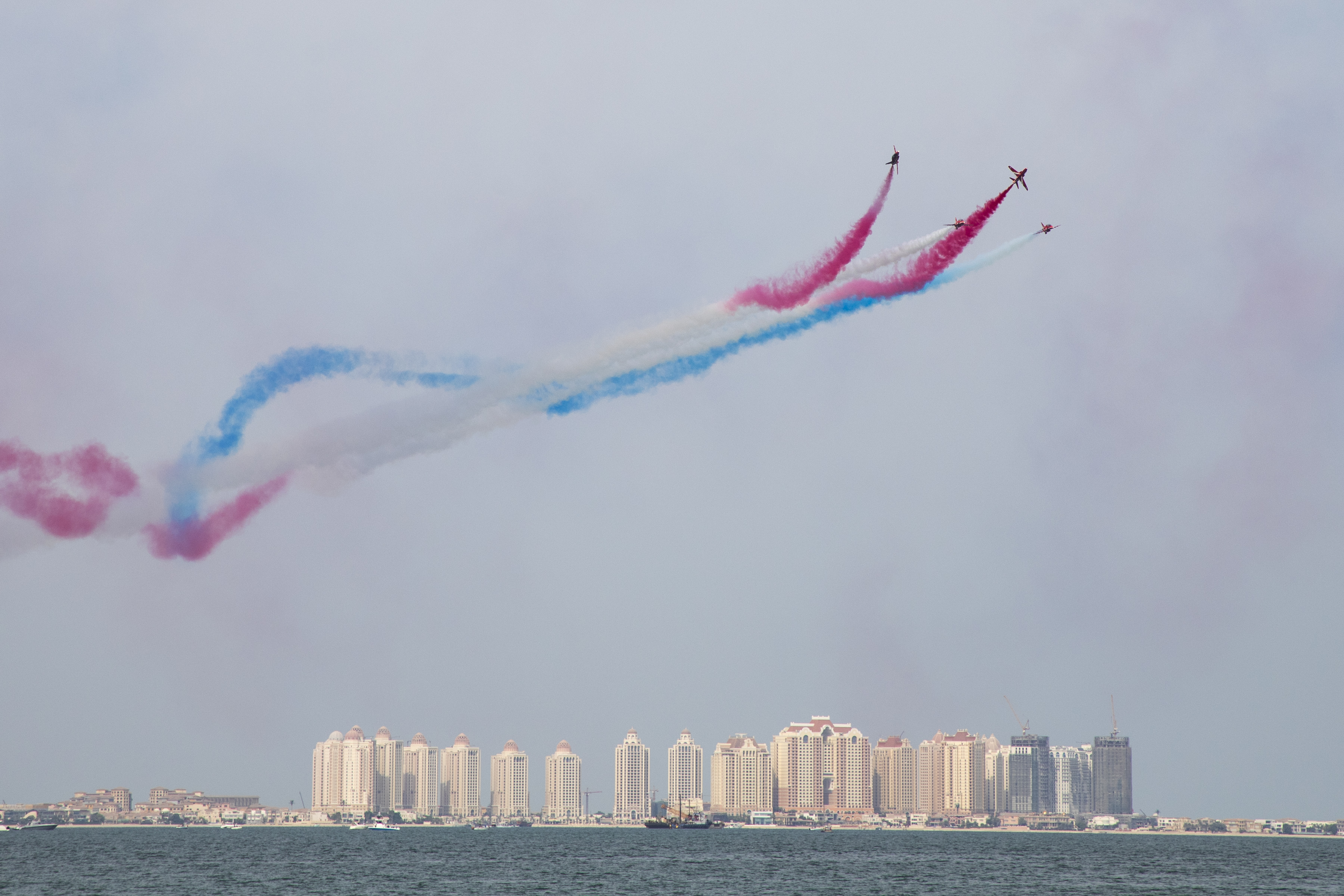Image shows Red Arrows performing with red, blue and white smoke trails over Qatar skyline.
